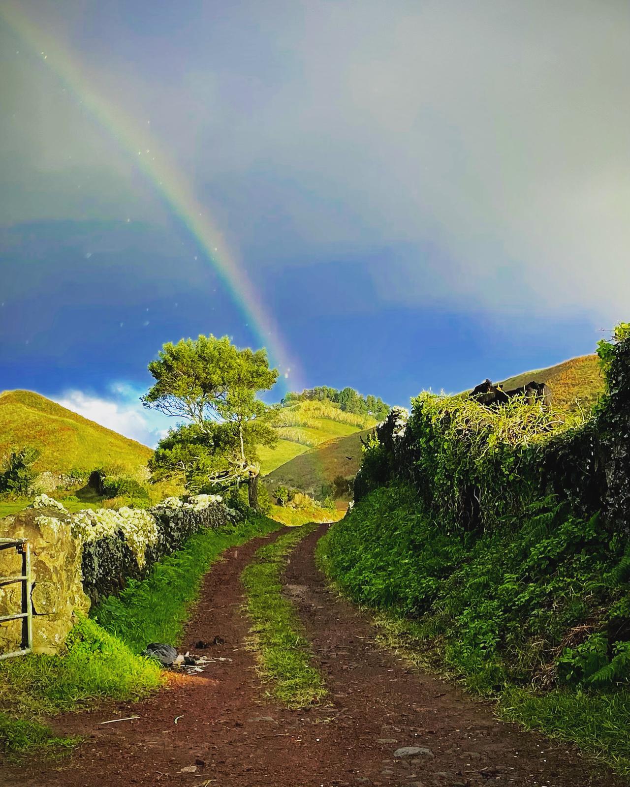 A rainbow above a rural path between stone walls and green hills in the Azores